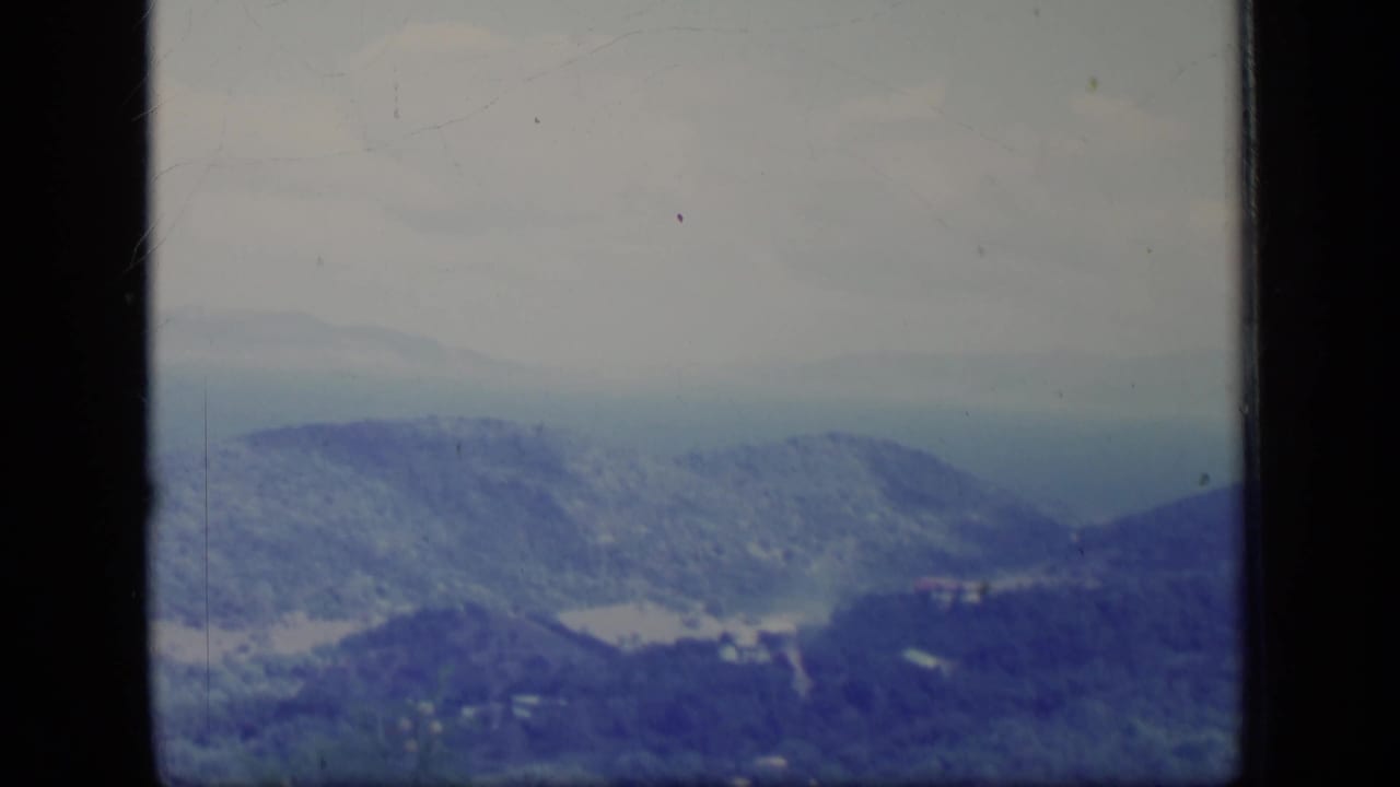 A soft 1970 Puerto Rico 8mm view of layered mountain ridges under hazy sky, with blue-purple color fading and dark film edges visible.