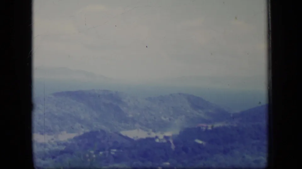 A soft 1970 Puerto Rico 8mm view of layered mountain ridges under hazy sky, with blue-purple color fading and dark film edges visible.