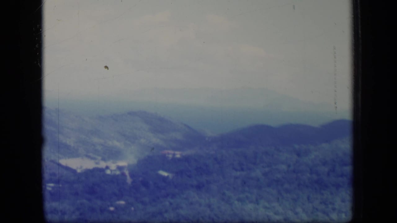 1970 Puerto Rico 8mm view of layered green mountains under a pale hazy sky, framed by dark film borders.