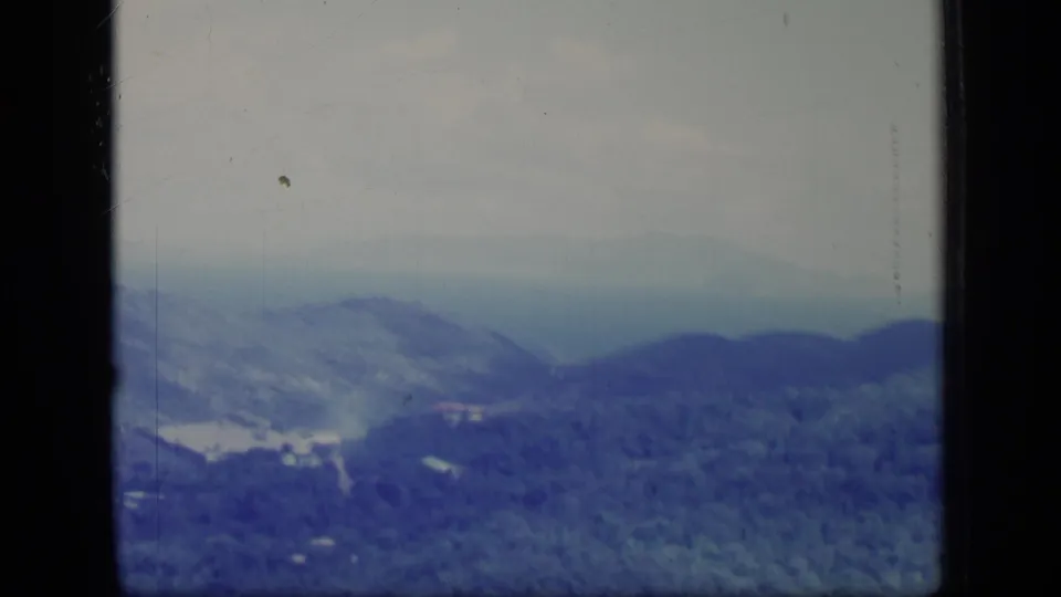 1970 Puerto Rico 8mm view of layered green mountains under a pale hazy sky, framed by dark film borders.