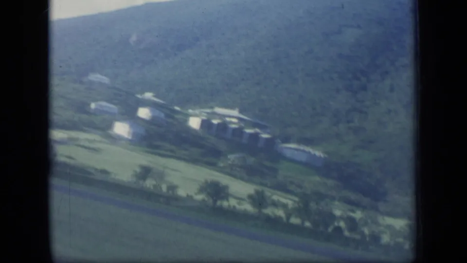 1970 Puerto Rico 8mm view of a rural settlement with white buildings, roads, fields, and a mountain backdrop.