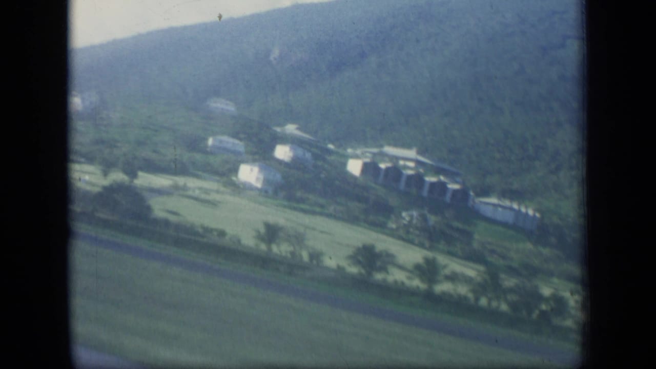 Aerial view of green hills with scattered pale buildings and fields.