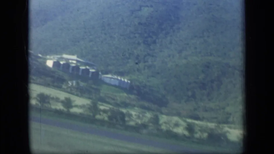 Aerial 8mm frame from Puerto Rico showing small hillside buildings, fields, and dense green mountain vegetation.