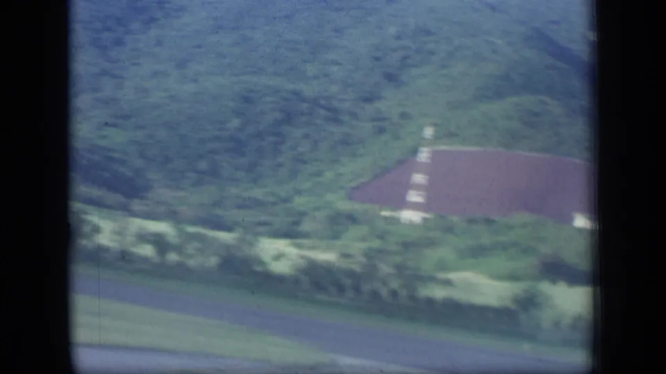 1970 Puerto Rico aerial view with a large red-roofed building, surrounding greenery, and a road crossing the lower frame.