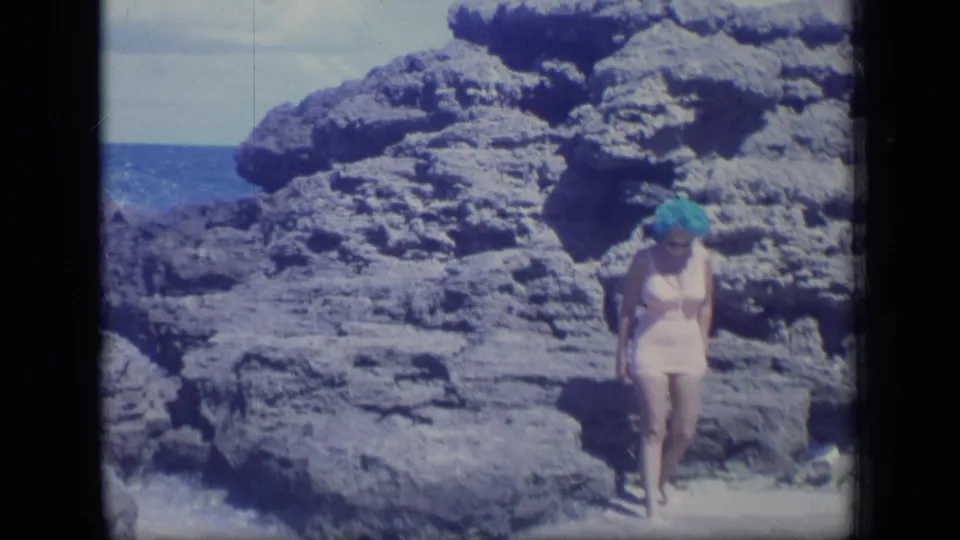 1970 Puerto Rico home-movie frame showing the woman stepping forward from coastal rocks toward the camera.