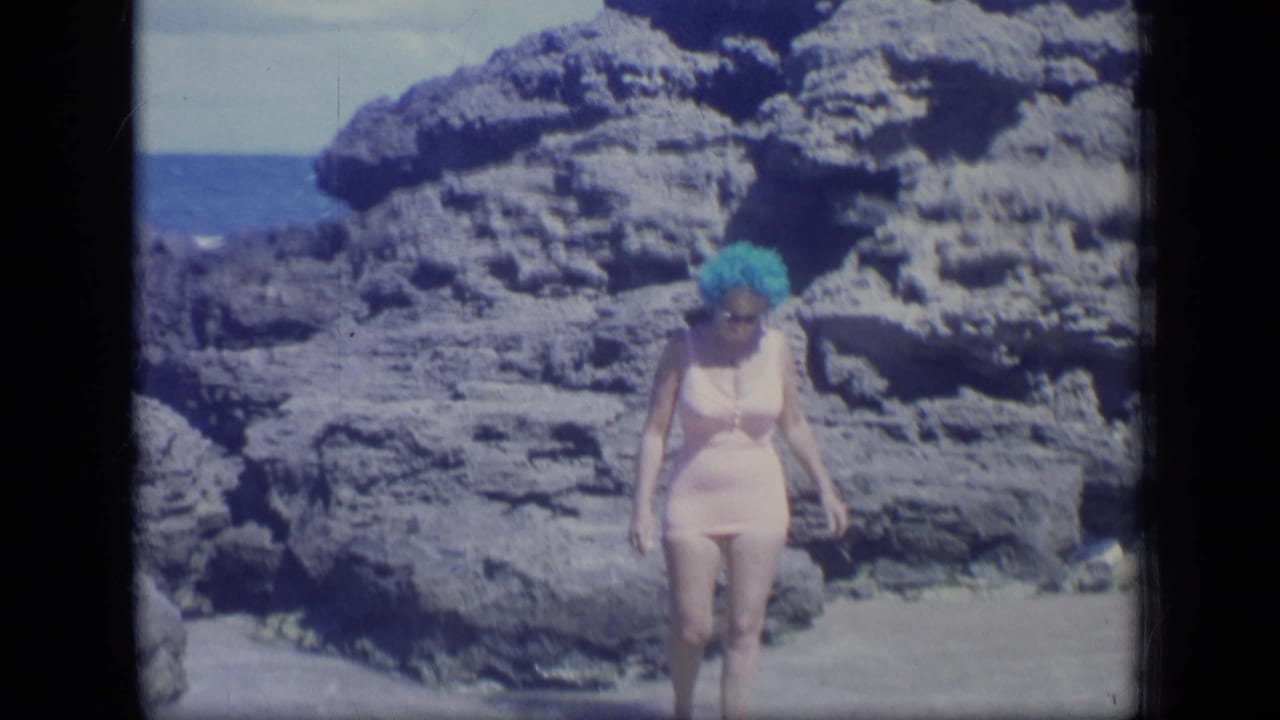The woman continues across shallow water on a rocky Puerto Rico beach, with the ocean visible beyond the stone formations.
