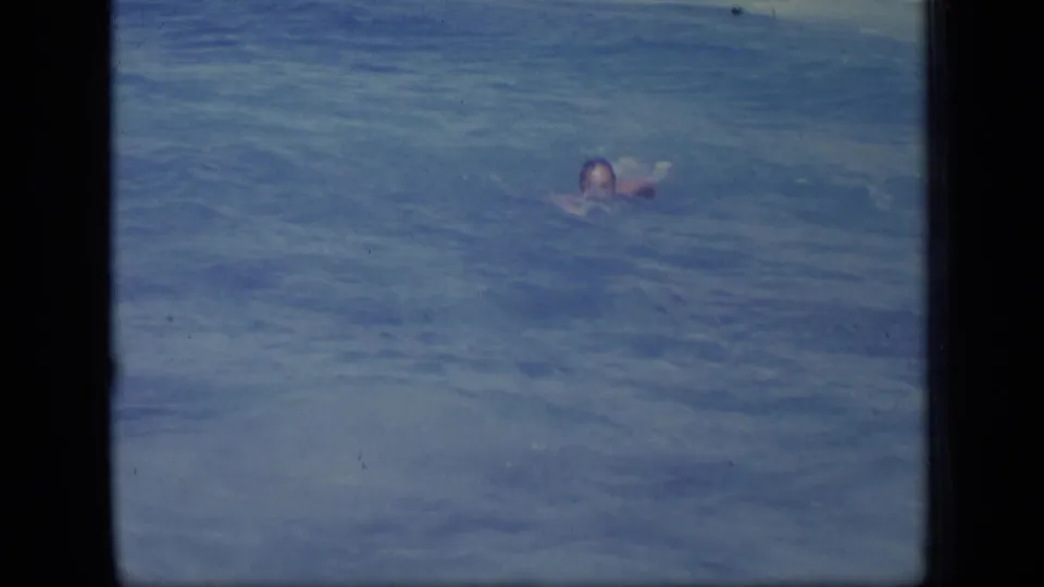 A swimmer is visible in blue Puerto Rico coastal water, framed from shore in grainy 1970 8mm home-movie footage.