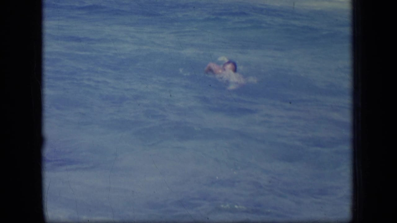 In 1970 Puerto Rico footage, a man swims in blue ocean water, seen at a distance within dark 8mm gate borders.