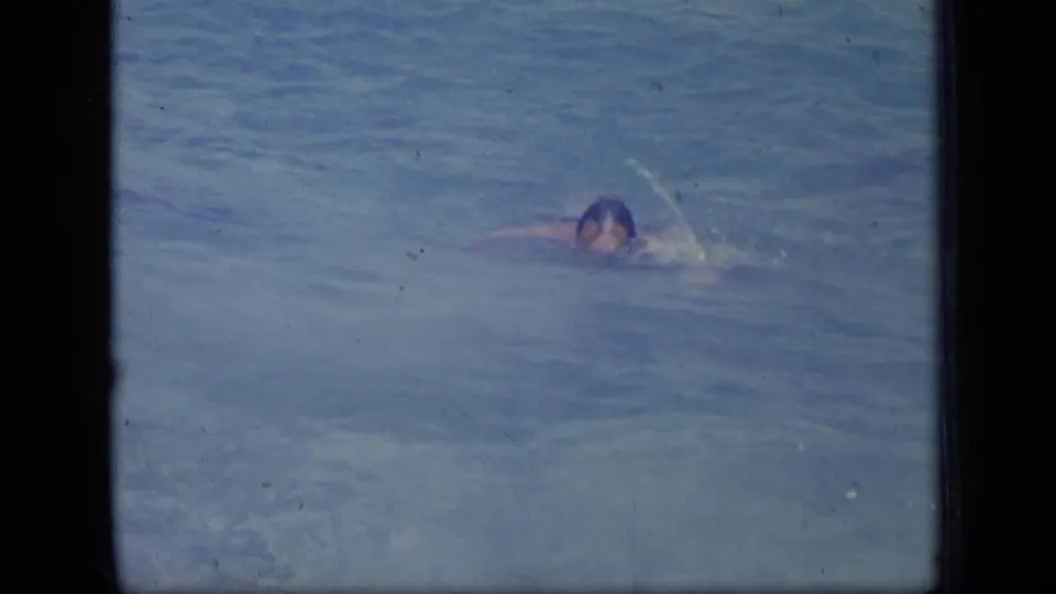 A man swims low in the blue ocean with one arm extended, framed by dark 8mm borders in 1970 Puerto Rico footage.