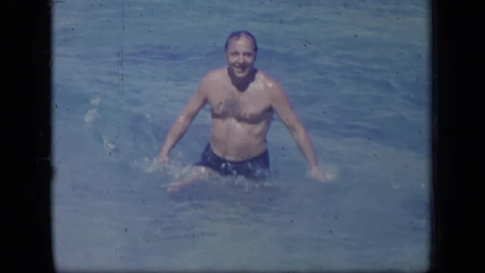 The man smiles toward the camera while standing in the ocean shallows in the 1970 Puerto Rico home-movie clip.