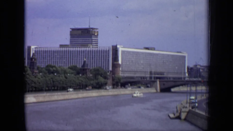 Wide 1971 Moscow riverside view with large modern buildings, a bridge, embankment, trees, water, and a small boat.