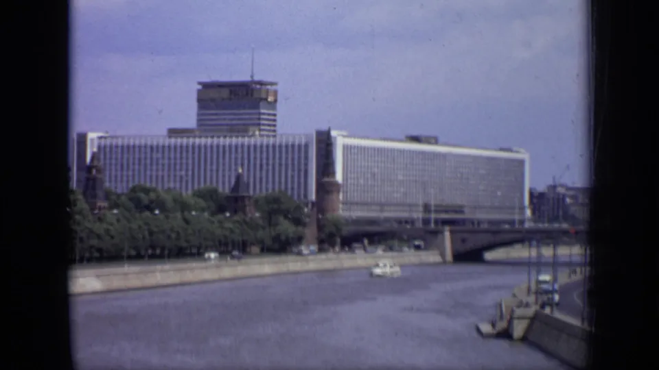 1971 Moscow riverfront view with Hotel Ukraina, bridge span, embankment trees, and a small boat on the water.
