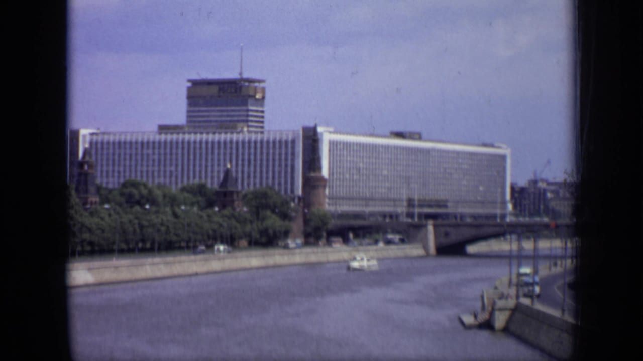 Riverfront hotel and bridge seen across the water with a small boat near the embankment.