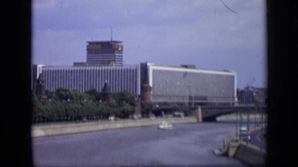 Soft 1971 8mm frame of Moscow's riverfront with Hotel Ukraina, bridge, tree-lined embankment, and boat on the water.