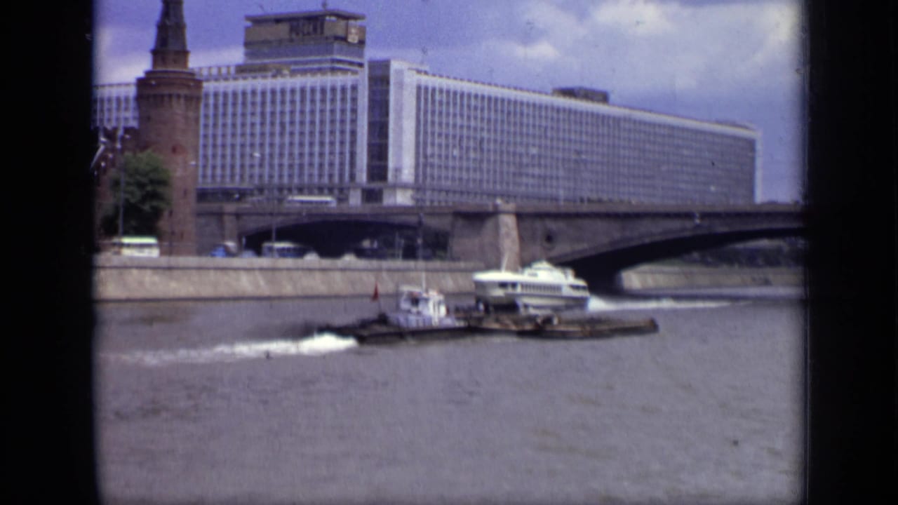 1971 Moscow river view with a white hydrofoil, tugboat, barge, bridge, Hotel Ukraina, and Kremlin tower in the background.