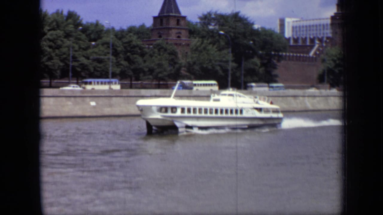 White hydrofoil boat traveling on a river with Kremlin walls and towers behind it.