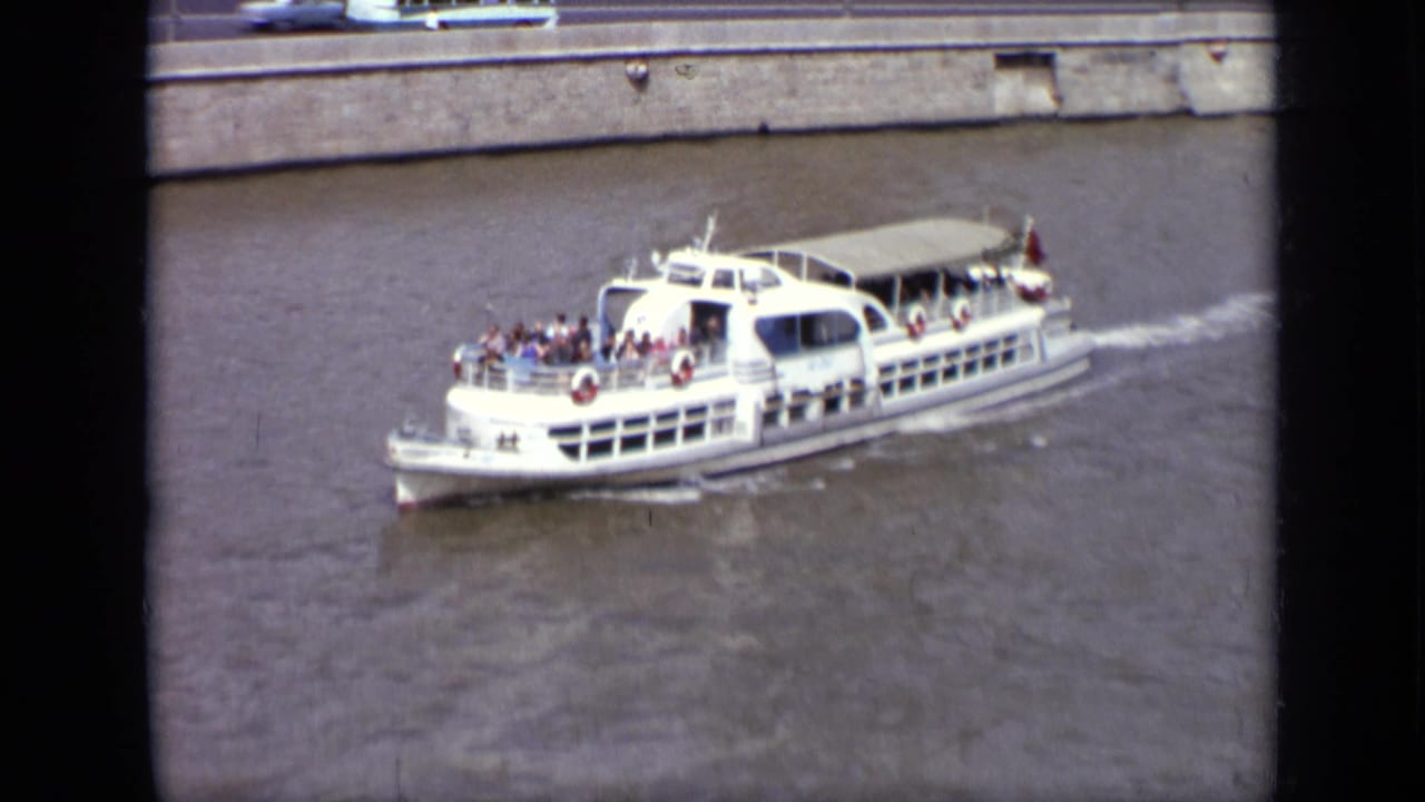 Close 1971 Moscow river view of a white excursion boat with passengers visible on deck near the embankment.