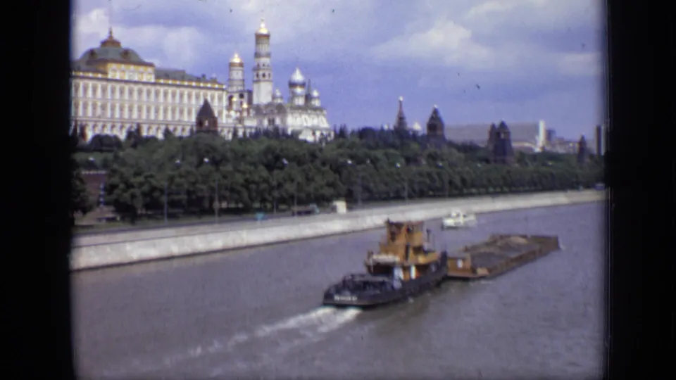 Soft 8mm frame of a tugboat and barge on the Moscow River, with Kremlin buildings and towers beyond the tree line.