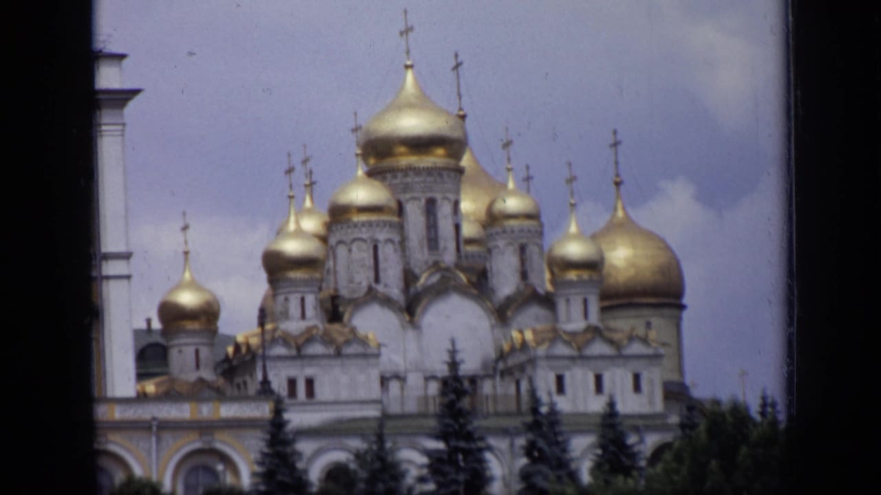 Golden onion domes and crosses above a white cathedral, partly framed by dark film edges.