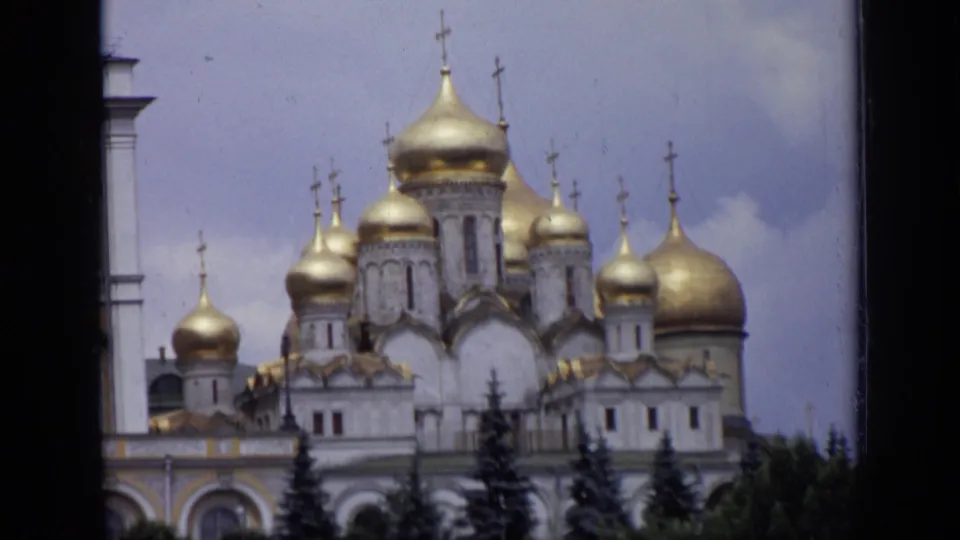 1971 Moscow 8mm frame showing golden domes, crosses, white cathedral walls, evergreens, and cloudy sky.