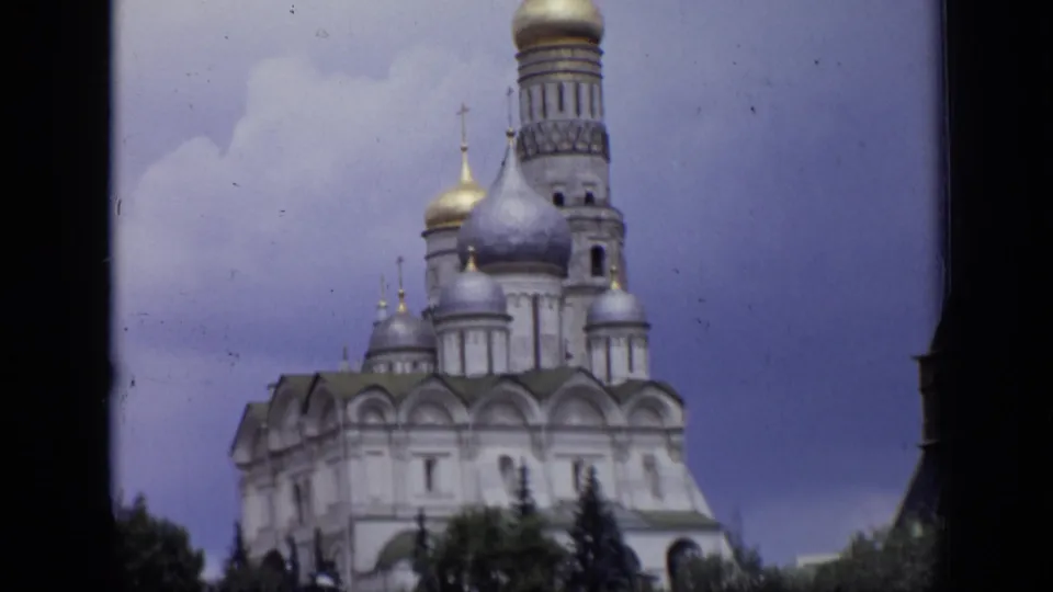 1971 Moscow 8mm frame of a cathedral tower, silver-toned and gold domes, white walls, and trees below.