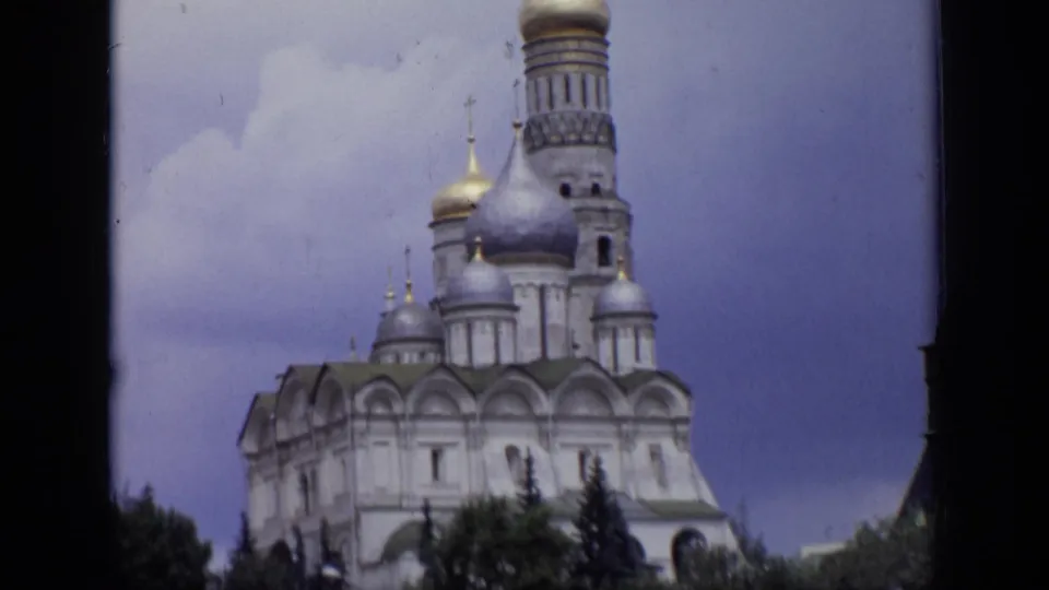 1971 Moscow home-movie frame showing a towered cathedral exterior with domes, crosses, trees, and dark film-edge framing.