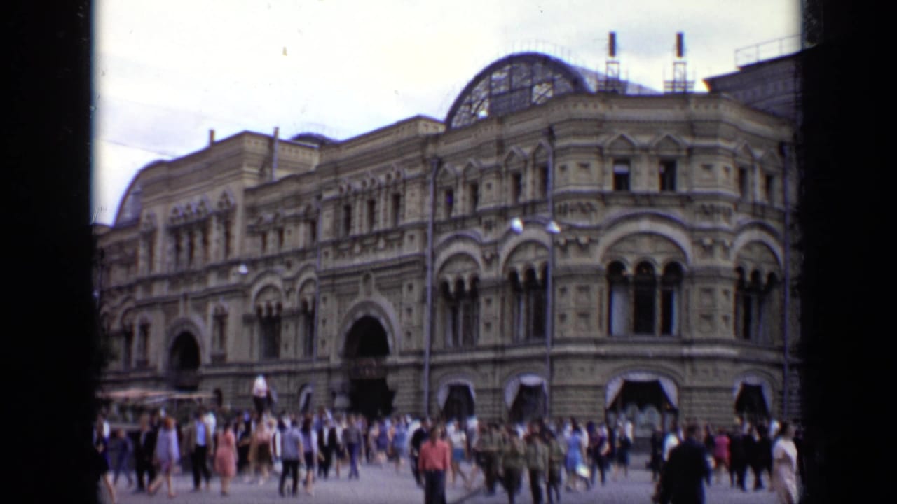 1971 Moscow home-movie frame showing visitors crossing a plaza before an ornate cultural landmark facade.