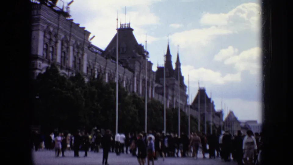 Moscow home-movie frame showing visitors in a public plaza with trees, lamp posts, and ornate buildings in the background.