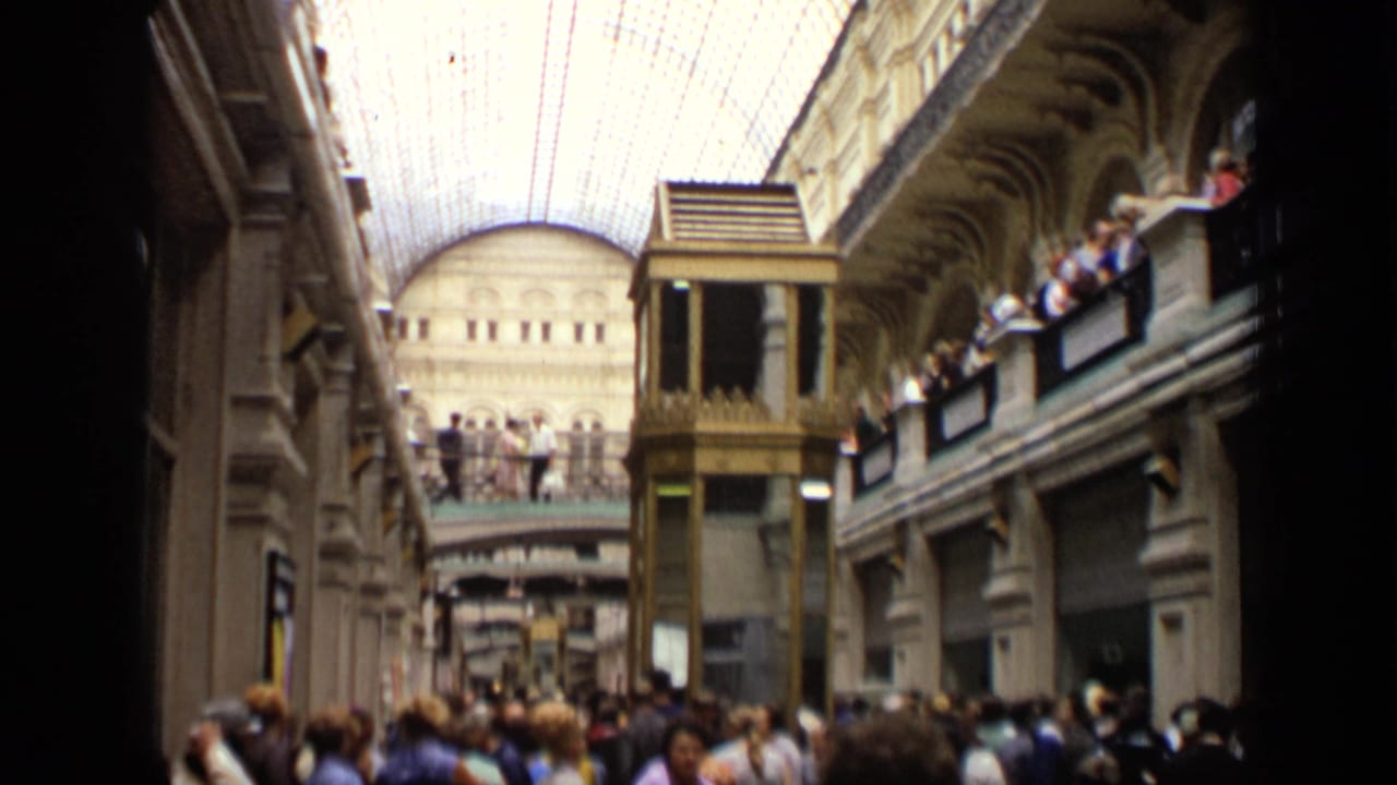 Busy arcade view with people on balconies, glass roof, and central elevator structure.