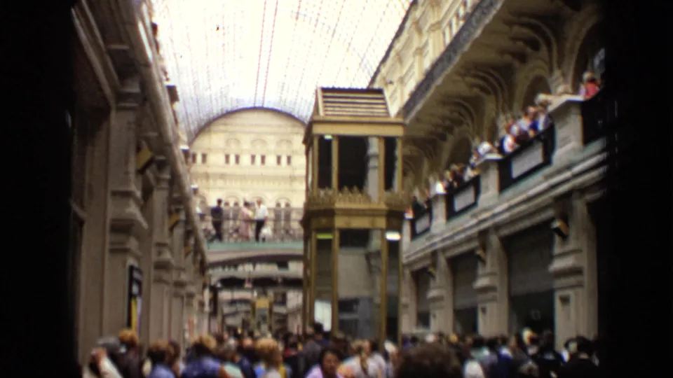 1971 Moscow arcade interior with a dense ground-floor crowd, balcony spectators, ornate arches, and a gold-toned elevator shaft.