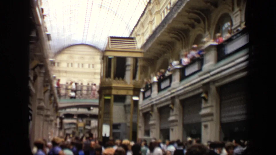 Soft 8mm frame of the Moscow arcade, with visitors filling the lower level and lining the upper balcony under the glass roof.