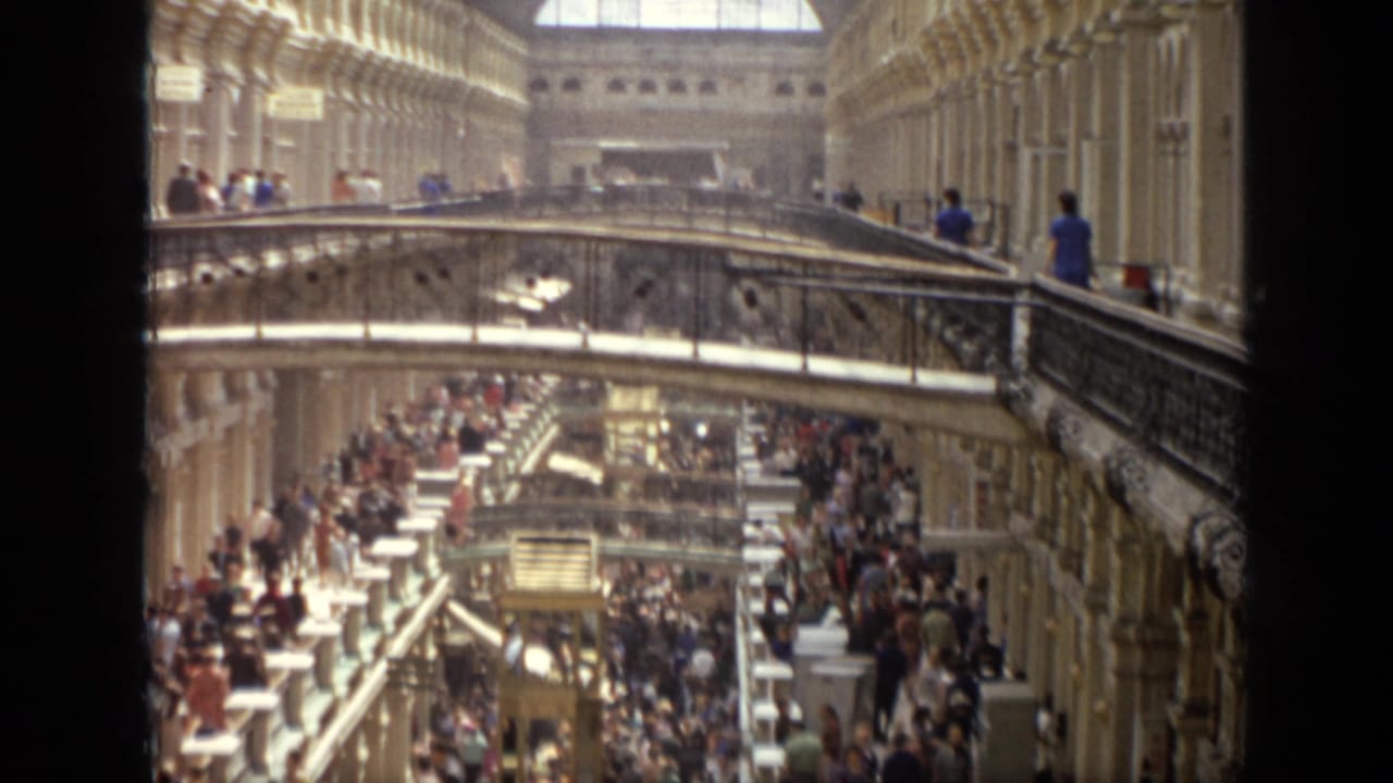 Crowded multi-level shopping arcade with arched interior and glass roof.