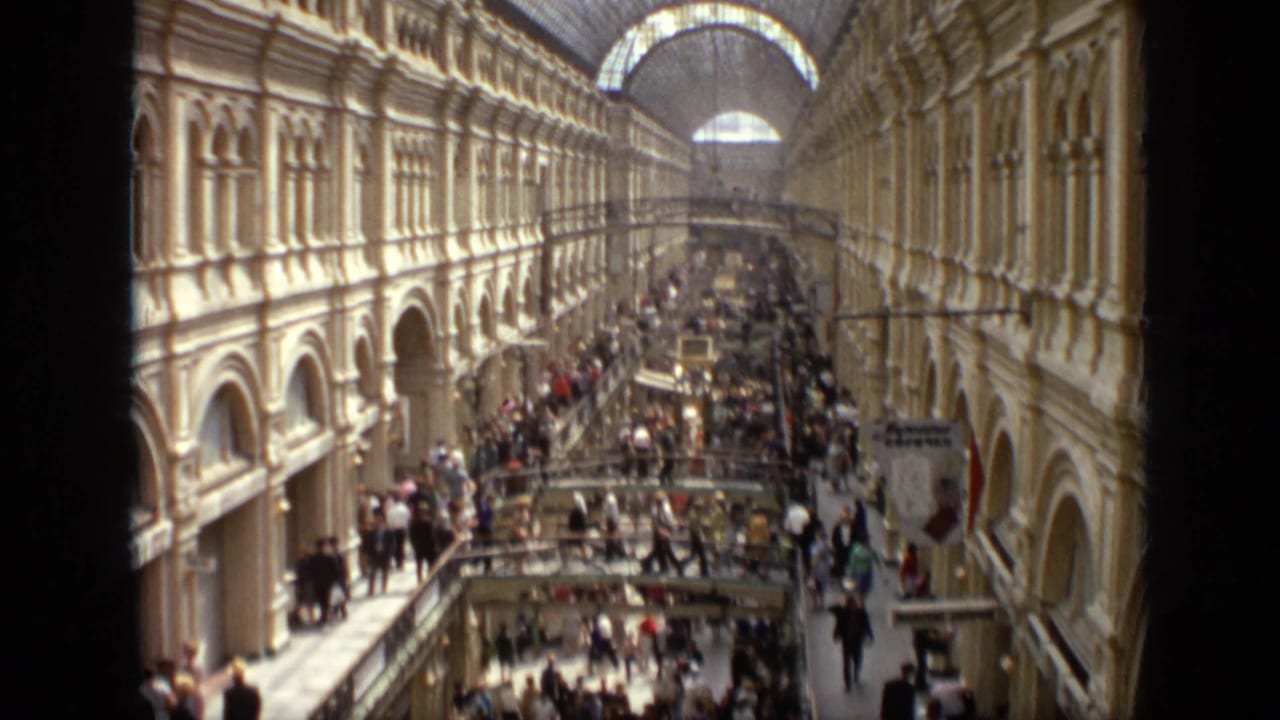Long arcade hall with crowds on multiple levels beneath a vaulted glass roof.