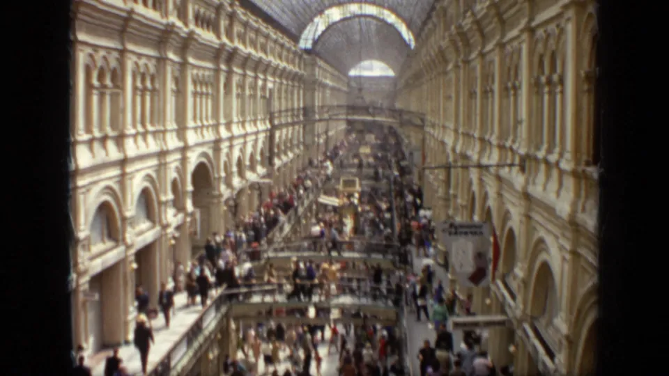 1971 Moscow 8mm frame of a crowded arcade interior with long balconies, arched walls, glass roof, and shoppers below.