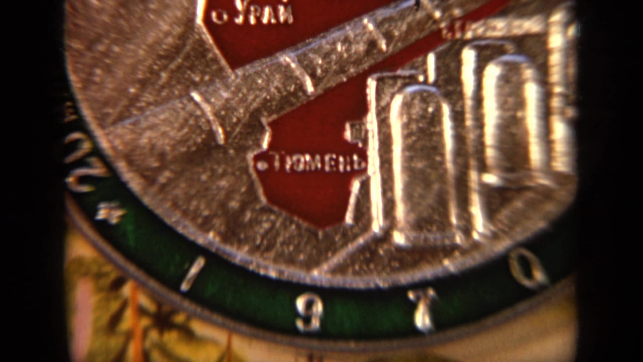 Tight 8mm close-up of the raised silver plate surface with red sections and partially readable Cyrillic lettering for Tyumen.