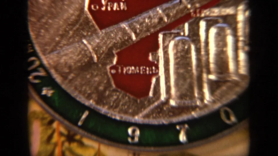 Tight 8mm close-up of the raised silver plate surface with red sections and partially readable Cyrillic lettering for Tyumen.