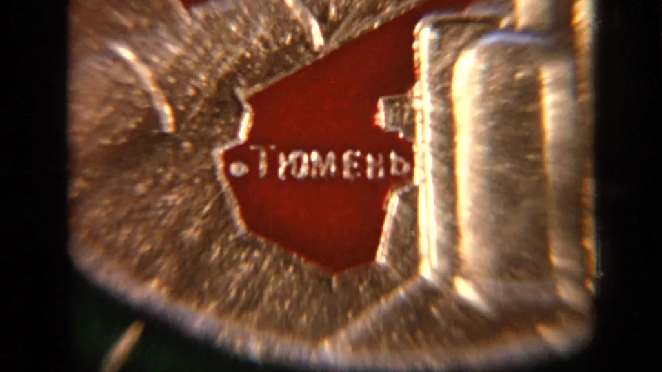 Extreme close-up of the red Tyumen section and polished raised metal forms on the Soviet industrial souvenir plate.