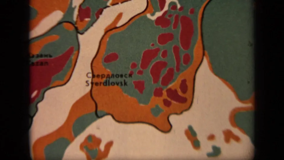 Extreme close 1971 8mm frame of the map near Sverdlovsk, emphasizing red patches, green areas, orange zones, and paper texture.