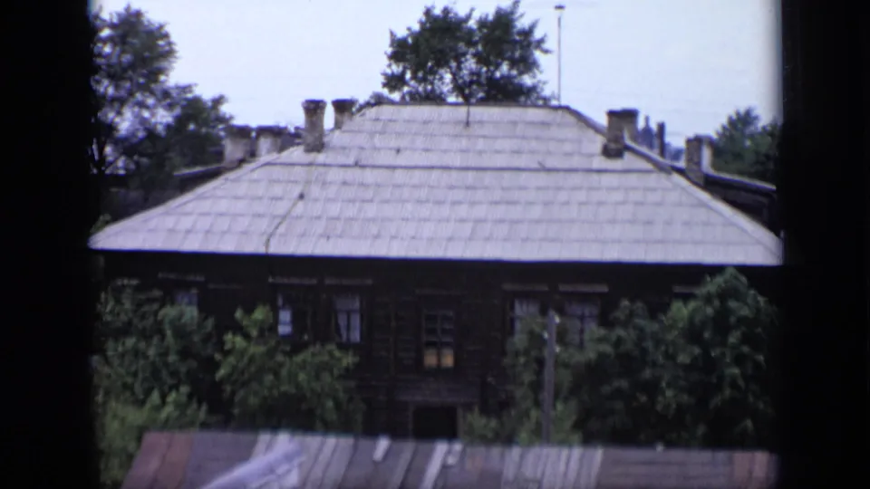 1971 Moscow residential exterior with a broad grey roof, multiple chimneys, leafy trees, and a dark window edge in the foreground.