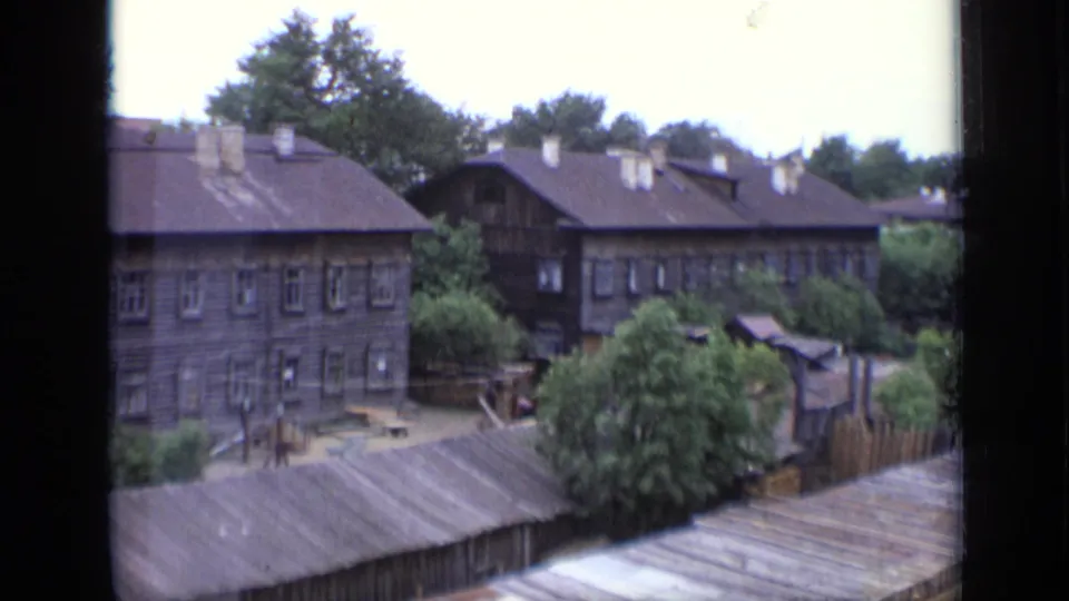 Wider 1971 Moscow home-movie view of wooden apartment buildings, rooflines, trees, fences, and a small courtyard area.