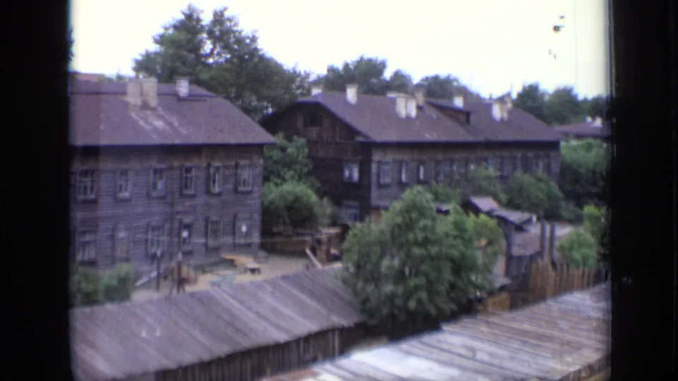 1971 Moscow residential scene showing wooden buildings with grey roofs and chimneys, leafy trees, fencing, and small yard structures.