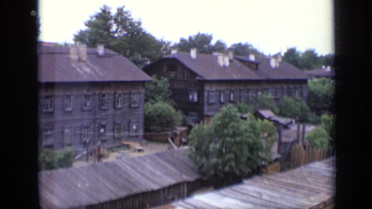 1971 Moscow home-movie view over wooden residential buildings, pitched roofs, chimneys, trees, and fenced yards.
