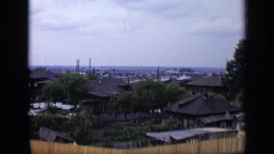 1971 Moscow home-movie view from a high vantage over residential rooftops, wooden fencing, trees and a distant city horizon.