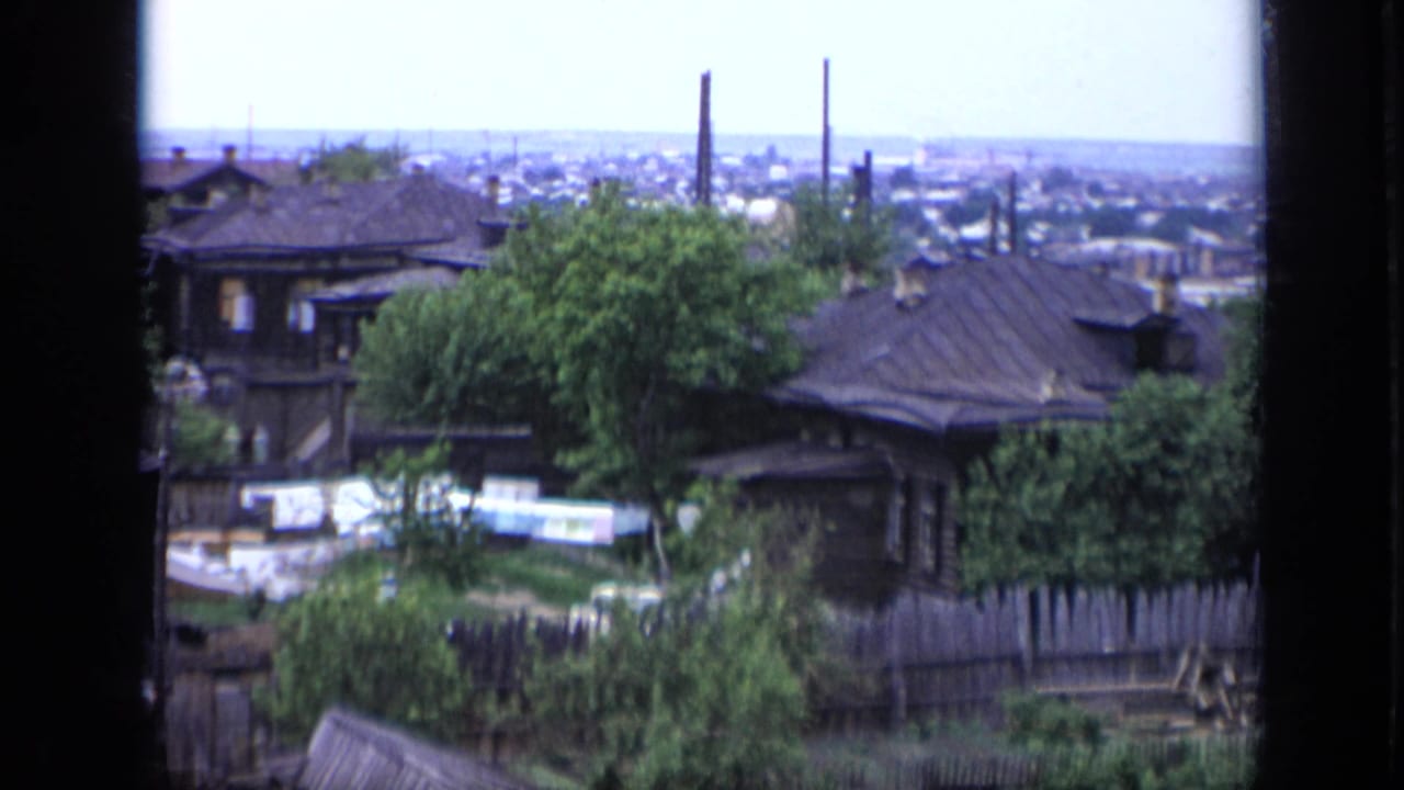 1971 Moscow residential view showing dark wooden houses, green trees, laundry lines, fences, and the city beyond.
