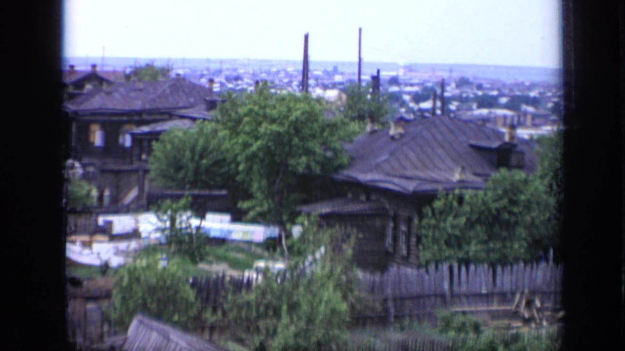 Elevated view across rooftops, greenery, and a hazy distant city horizon.