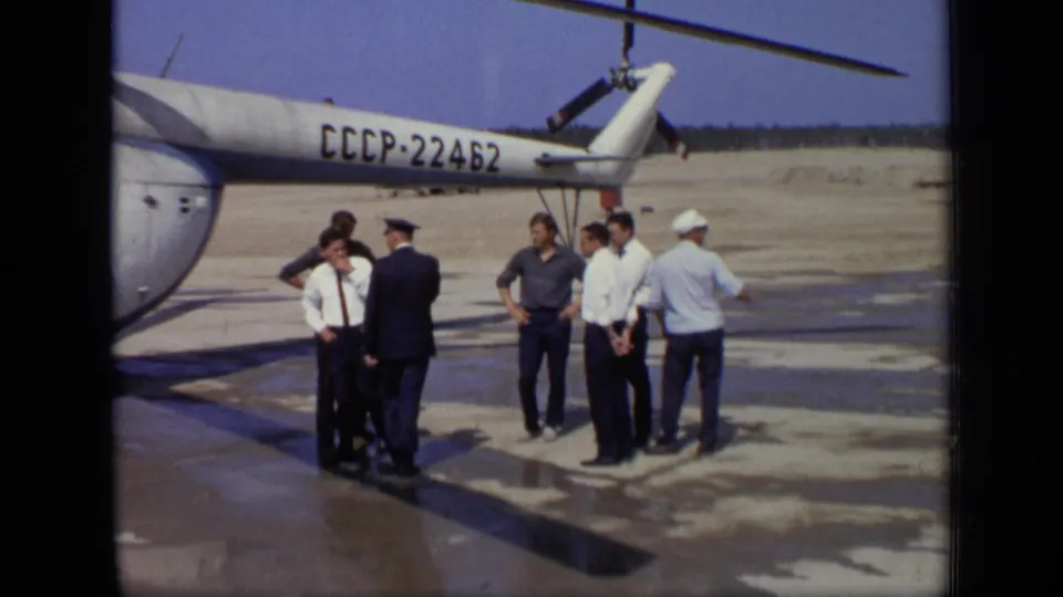 Several adults gather beneath the tail of a Soviet helicopter marked CCCP-22462 on a wet helipad area.