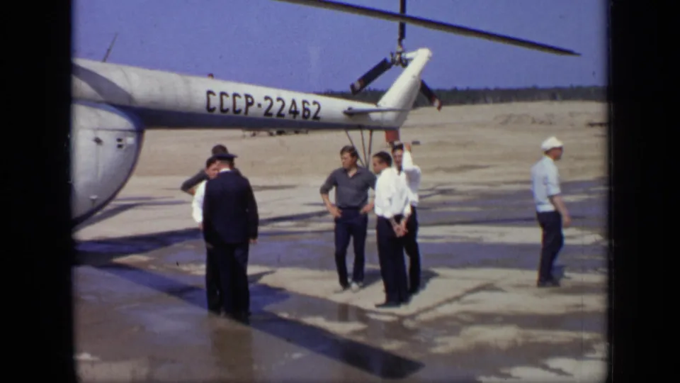 In the 1971 Moscow clip, adults stand near a Soviet helicopter tail on a damp open landing area.