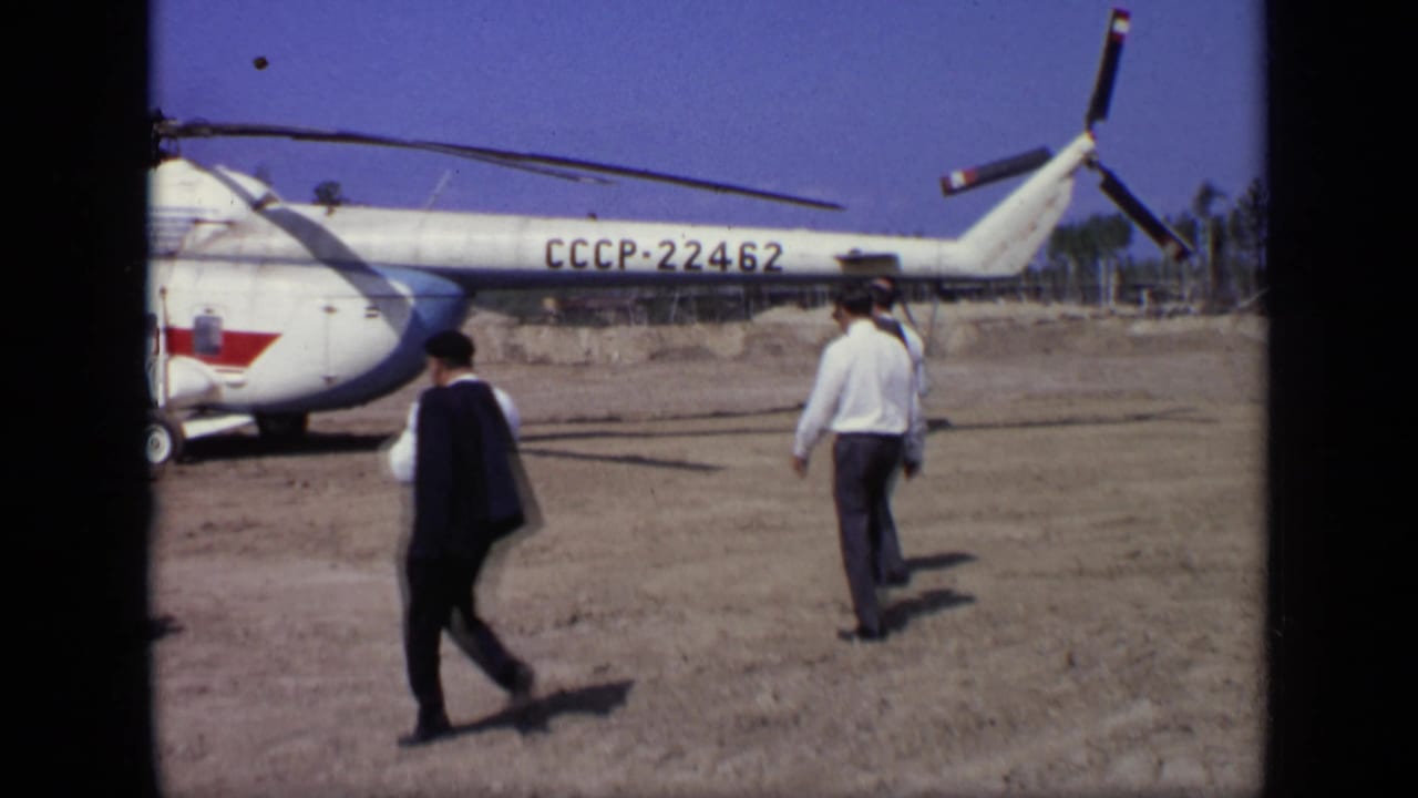 In 1971 Moscow footage, suited men walk toward a white Soviet helicopter marked CCCP-22462 on a dry open airfield.