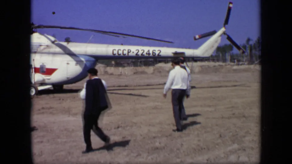 In 1971 Moscow footage, suited men walk toward a white Soviet helicopter marked CCCP-22462 on a dry open airfield.