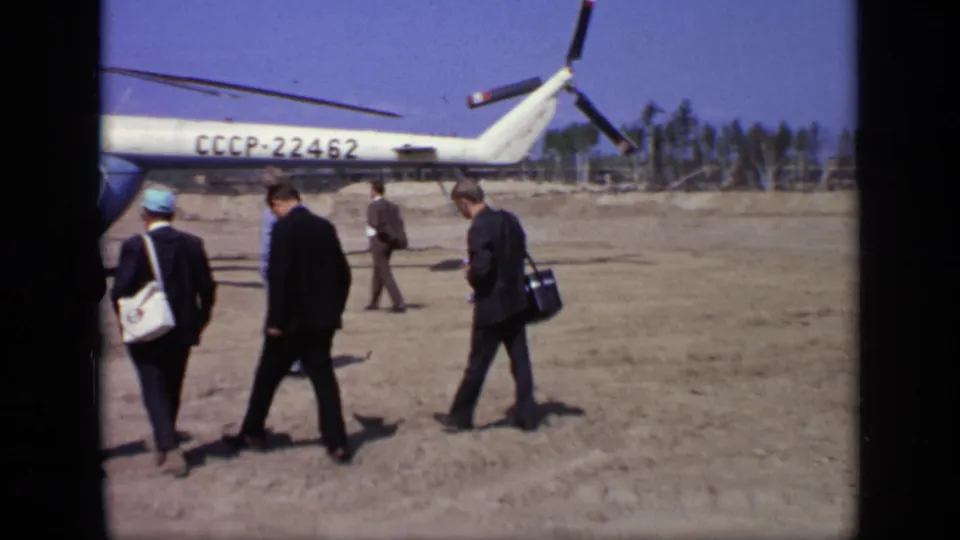 Men in formal clothing, including one with a shoulder bag, walk beside the CCCP-22462 helicopter in the 1971 Moscow airfield scene.